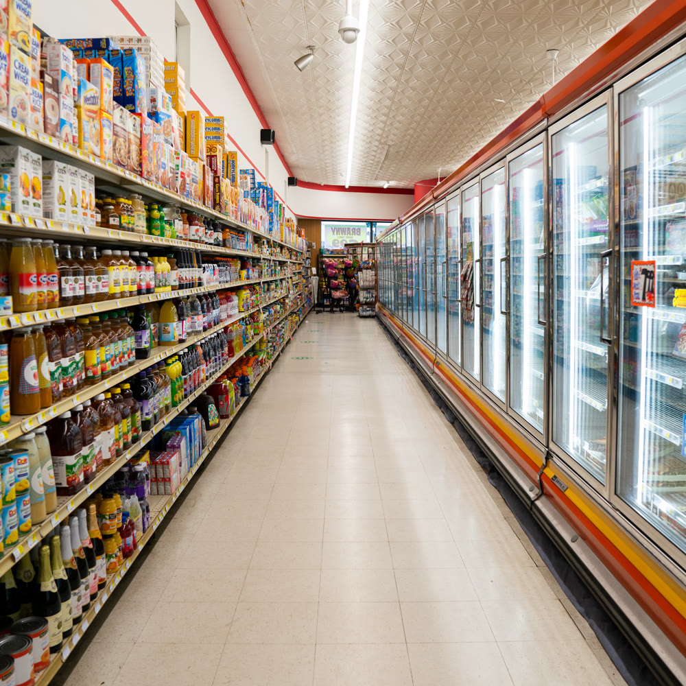 A bright, clean grocery aisle with full shelves on the left and freezer doors on the right